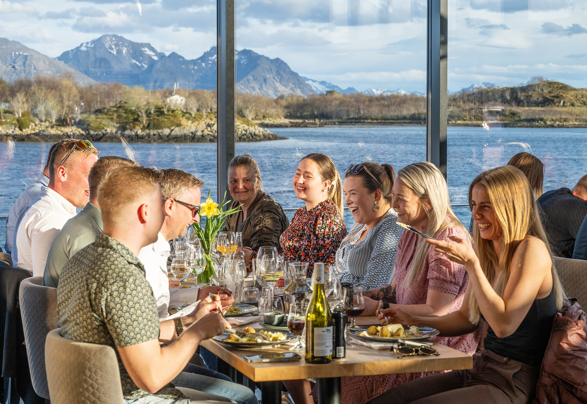 Group of guests dining together indoors with sea and mountain views at Ringstad Resort
