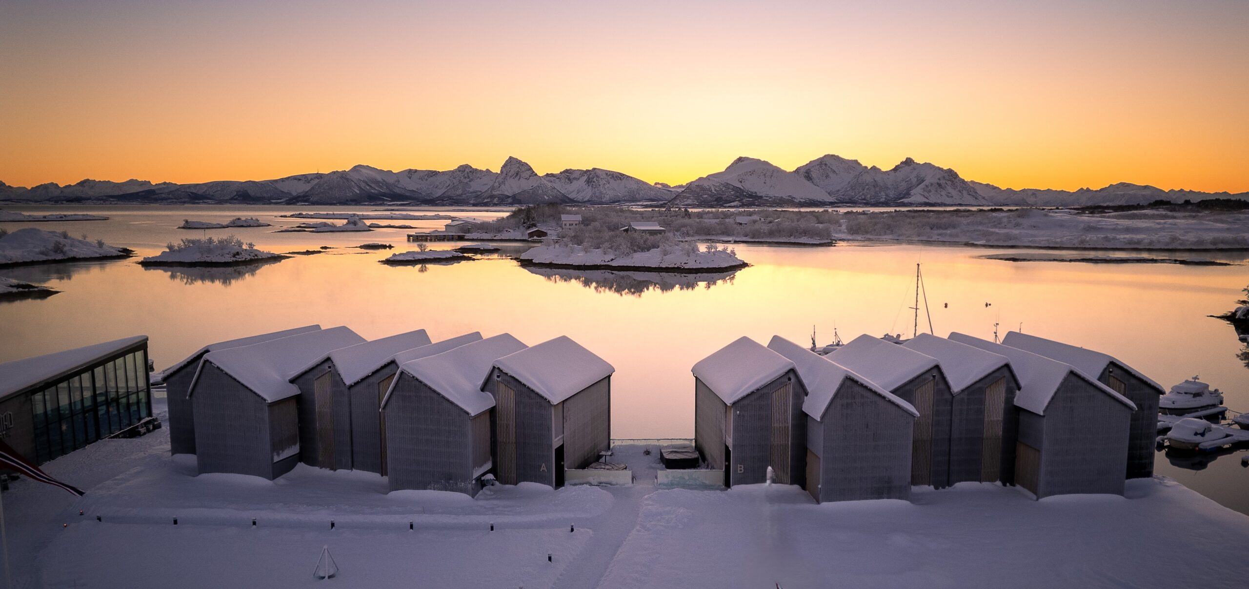 Ringstad Resort by the sea at sunset with snow-covered buildings and mountains