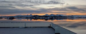 Snow-covered mountains reflected in calm Arctic waters near Ringstad Resort at sunset