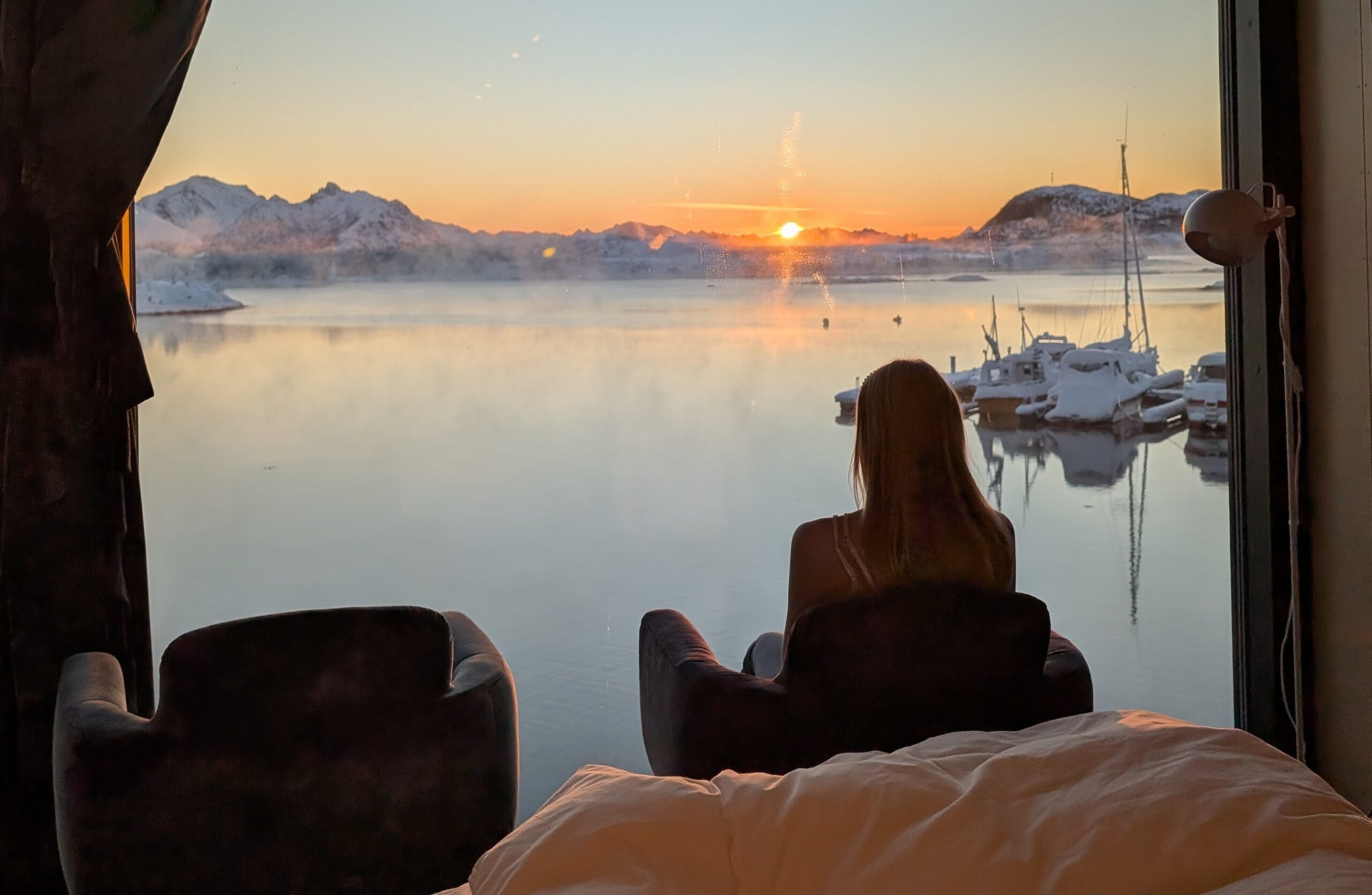 Guest sitting indoors watching the winter sunrise over calm Arctic waters at Ringstad Resort
